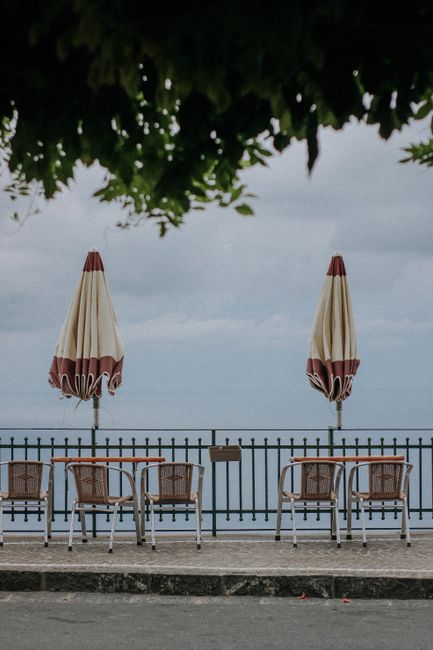 Empty chairs and closed umbrellas at a seaside cafe with ocean view.