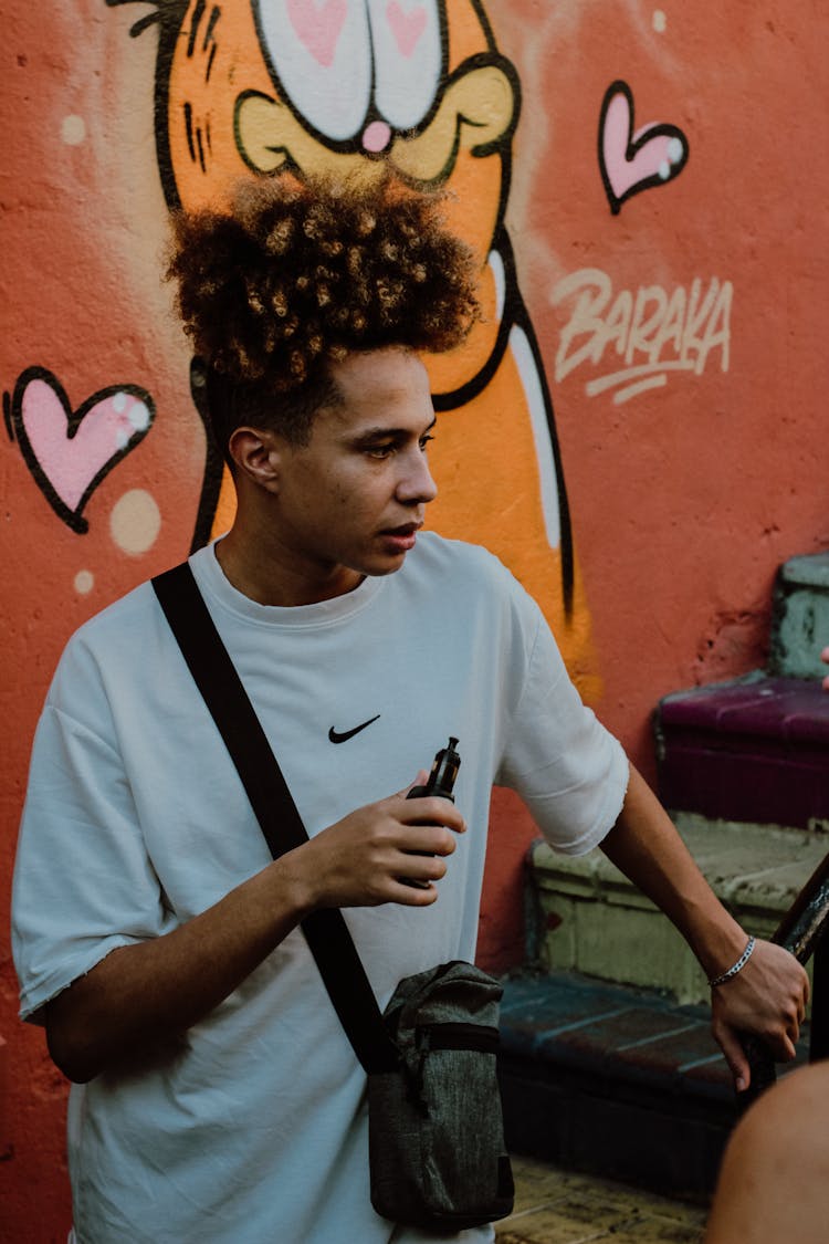 A Man With Curly Hair Holding A Vape