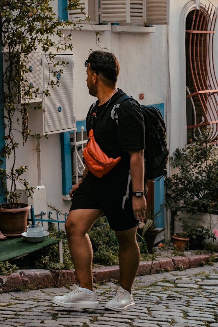 A Man In A Black Outfit Carrying A Backpack And A Cross Body Bag