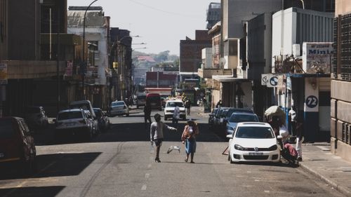 Free A dynamic street scene in Johannesburg capturing daily life with parked cars and people walking. Stock Photo