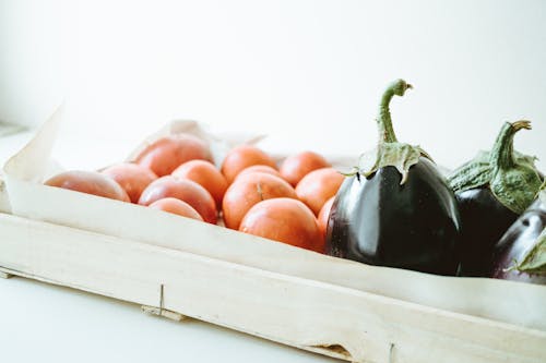 Close-up Photo of Purple Eggplants and Round Orange Fruits