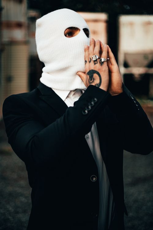 Free A person in a black blazer and balaclava with tattoos, posing outdoors. Stock Photo