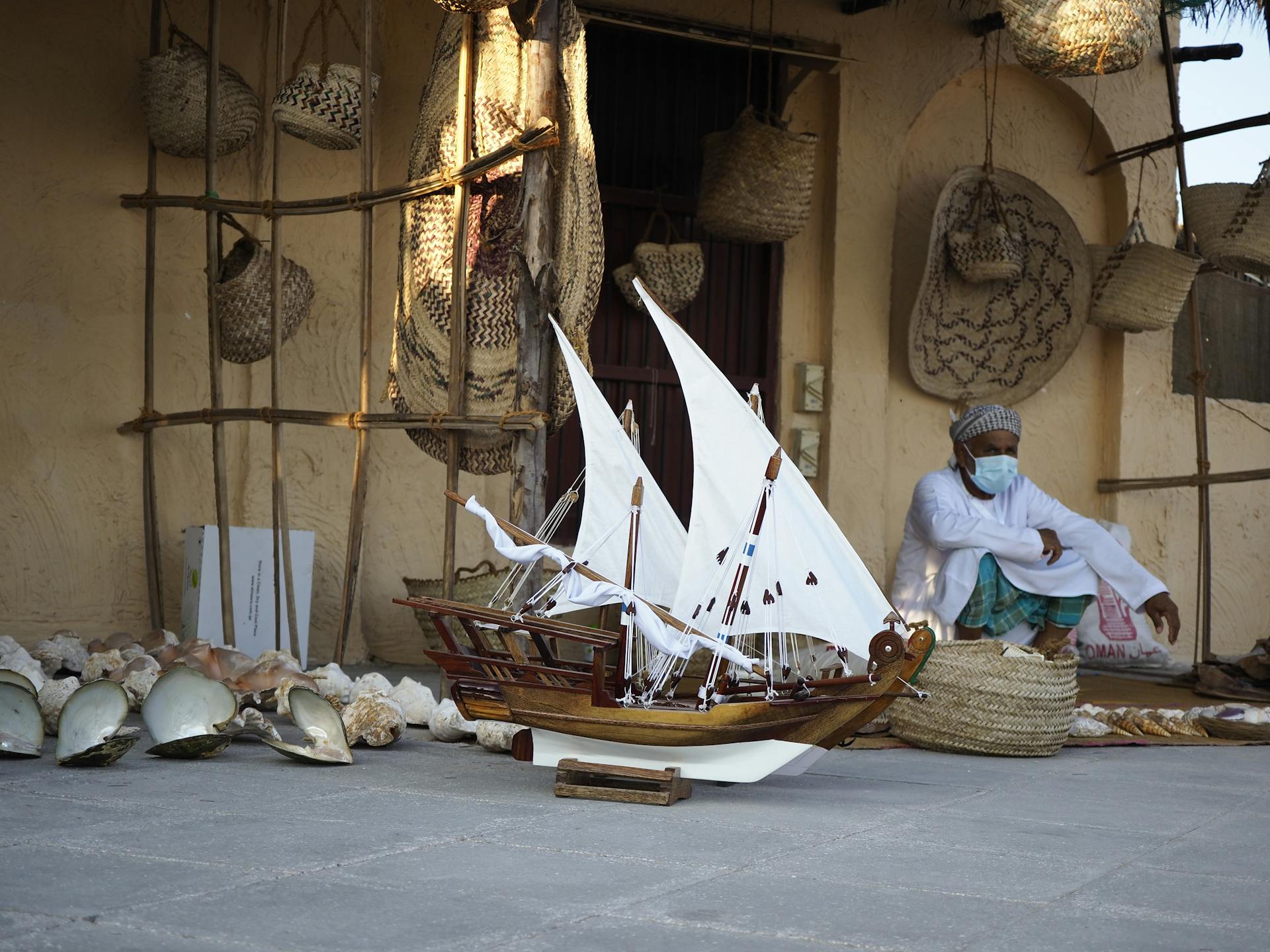 A Model Ship beside a Man in a Thobe