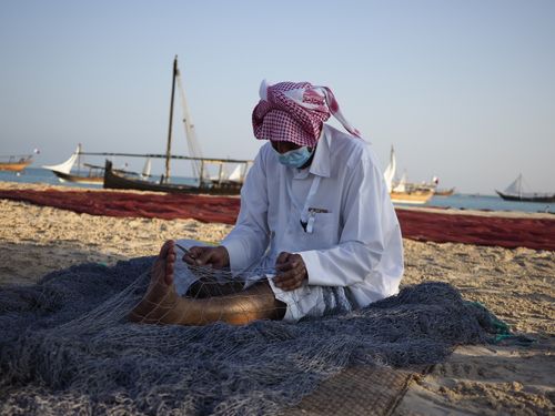 Free A traditional fisherman repairs nets on a beach in Doha, Qatar. Stock Photo
