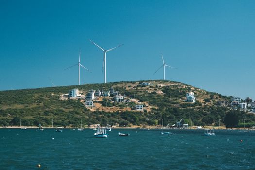 Wind turbines on a coastal hill overlooking the sea on a clear day, showcasing alternative energy and natural beauty.