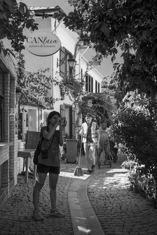 Grayscale Photo of a Woman Taking a Photo while Outside a Building