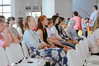 A diverse group of people sitting attentively during an indoor meeting or event, captured in a spacious room.