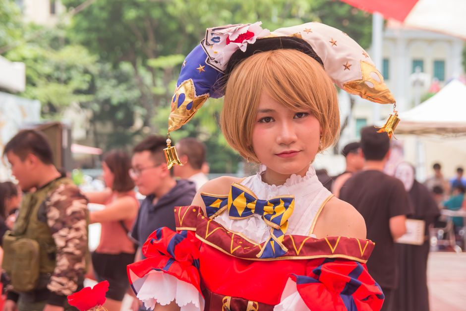 Young woman in elaborate costume at a vibrant outdoor festival showcasing cosplay culture.