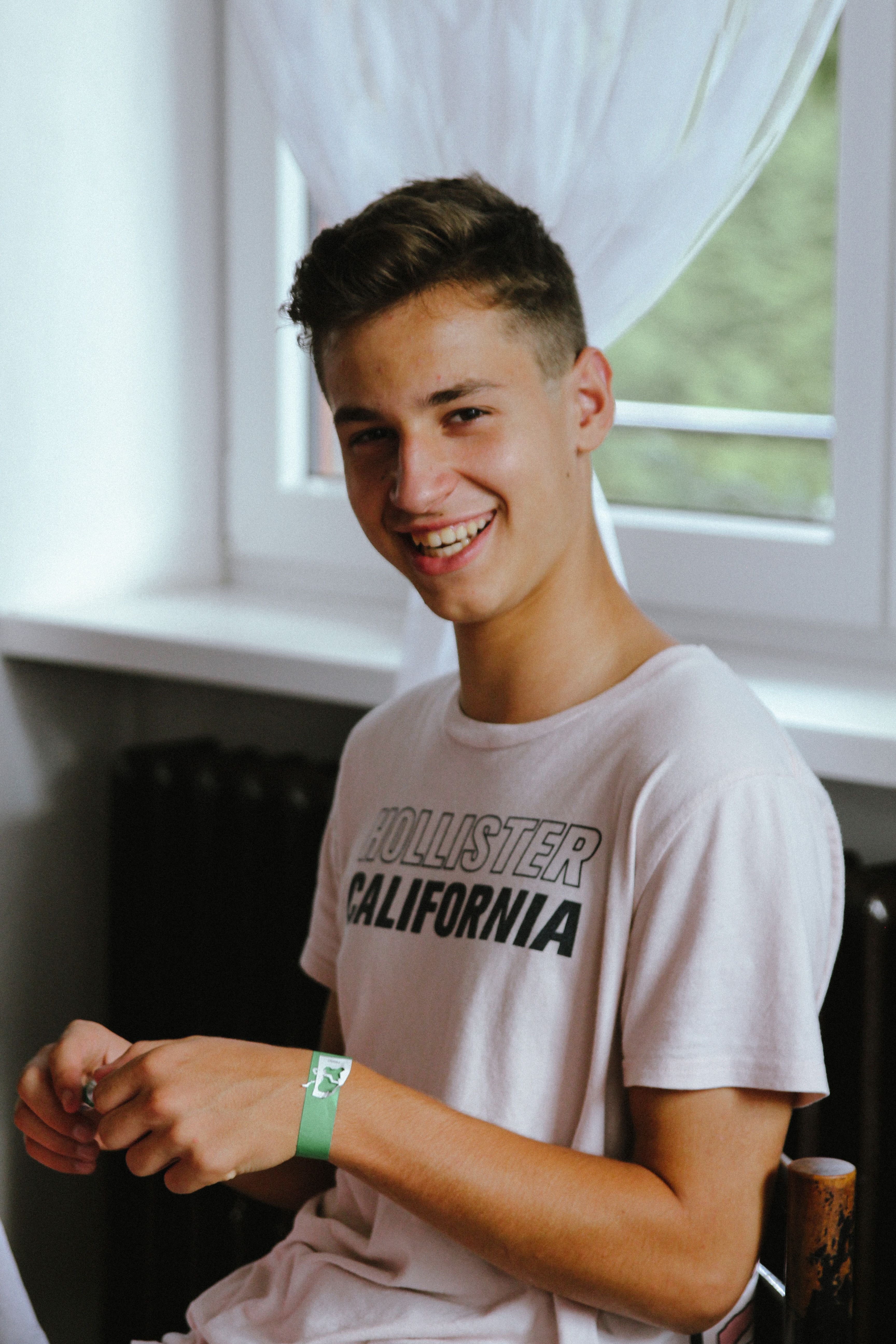 A cheerful teenage boy smiling indoors, wearing a casual white t-shirt.