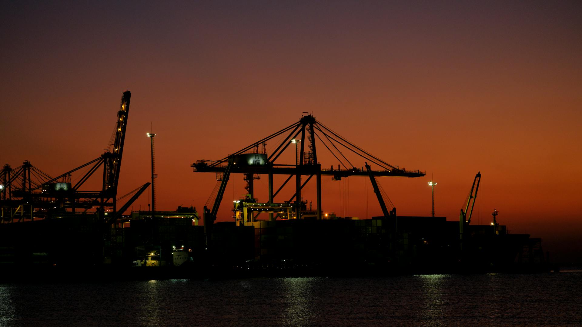 Silhouetted port cranes with a sunset background, highlighting trade and commerce at the waterfront.