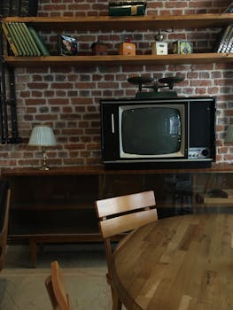 Cozy vintage room featuring a retro TV, brick wall, wooden table, and shelves with books.