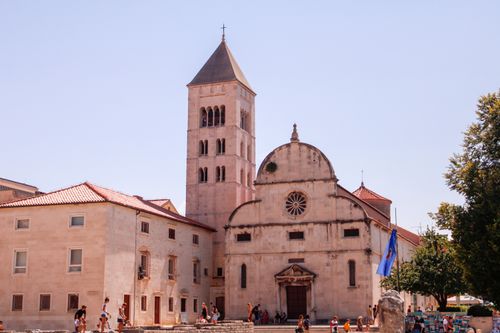 Free A historic church exterior under a bright summer sky, surrounded by tourists exploring the vibrant square. Stock Photo
