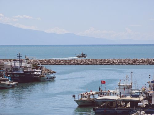 Free A sunlit harbor scene featuring fishing boats moored along the pier with distant mountains. Stock Photo