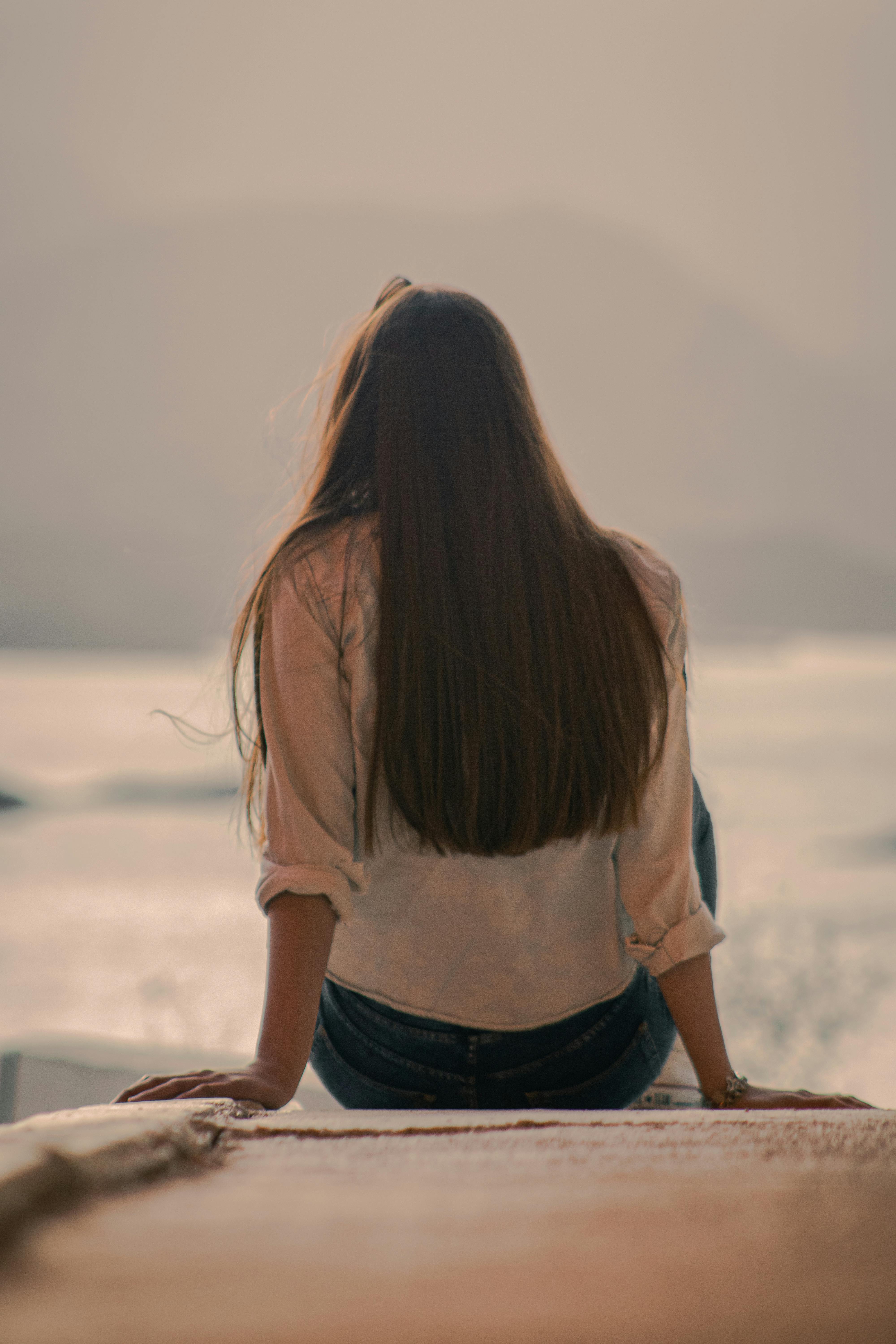 Rear view of a woman with long hair sitting by a serene lake, Potrerillos, Argentina.