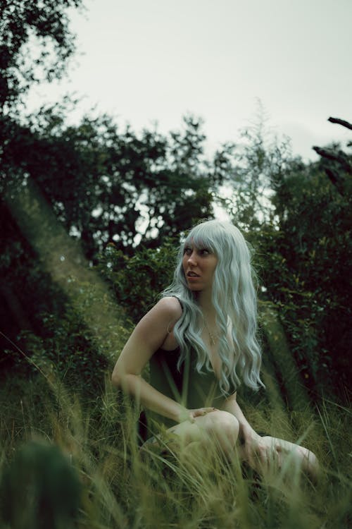 Woman with Long White Hair Sitting on Green Grass