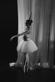 Black and white photo of a ballerina dancing gracefully next to a curtain indoors.