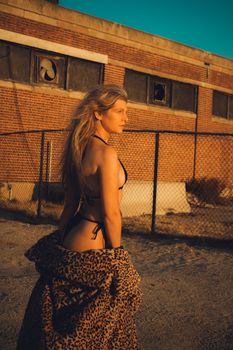 A fashionable woman poses outdoors at sunset in Asbury Park wearing a leopard print coat.