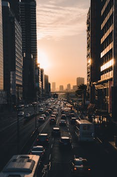 A bustling city street with heavy traffic during sunset. High-rise buildings framing the scene.