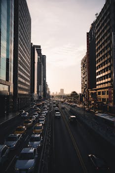 A bustling city street framed by towering skyscrapers during a vibrant sunset, capturing urban life in motion.