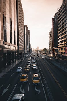 An aerial view of city traffic on a busy street during sunset, flanked by skyscrapers.