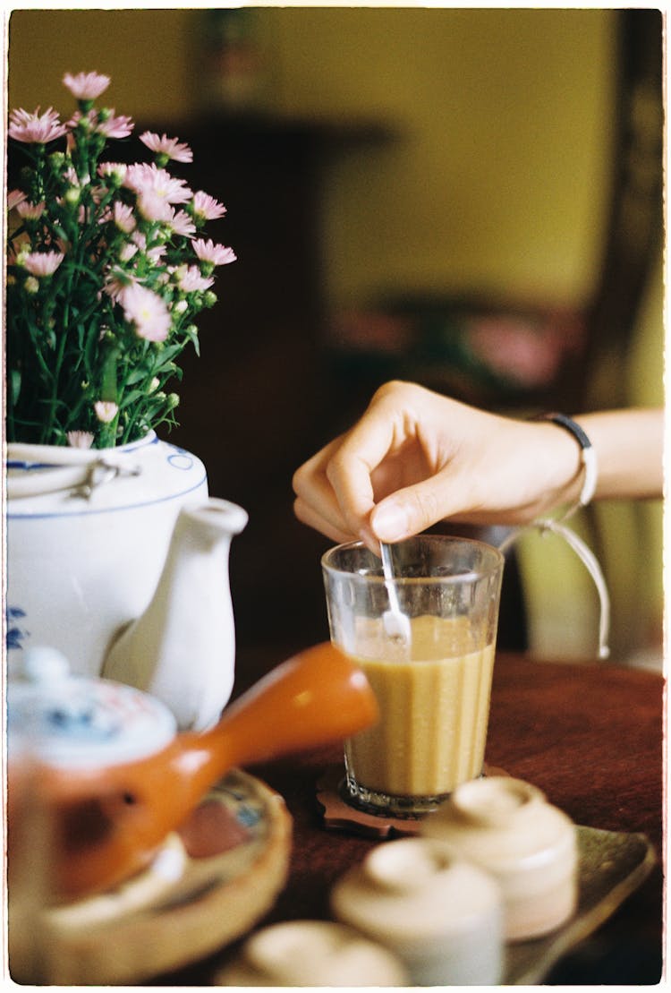 Hand Of A Person Stirring Brown Liquid In A Clear Glass