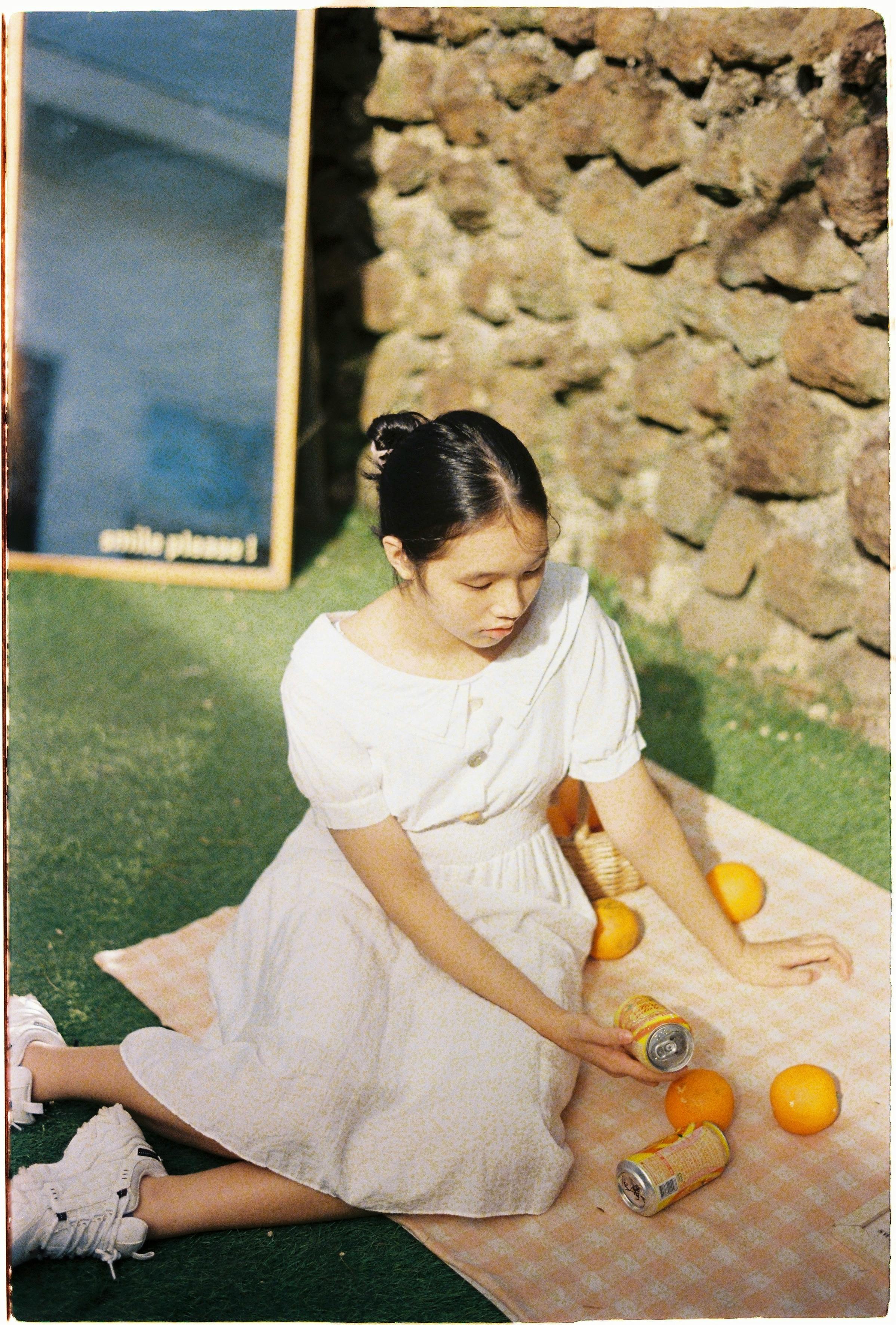 Teen girl enjoying an outdoor picnic with oranges on a sunny day.