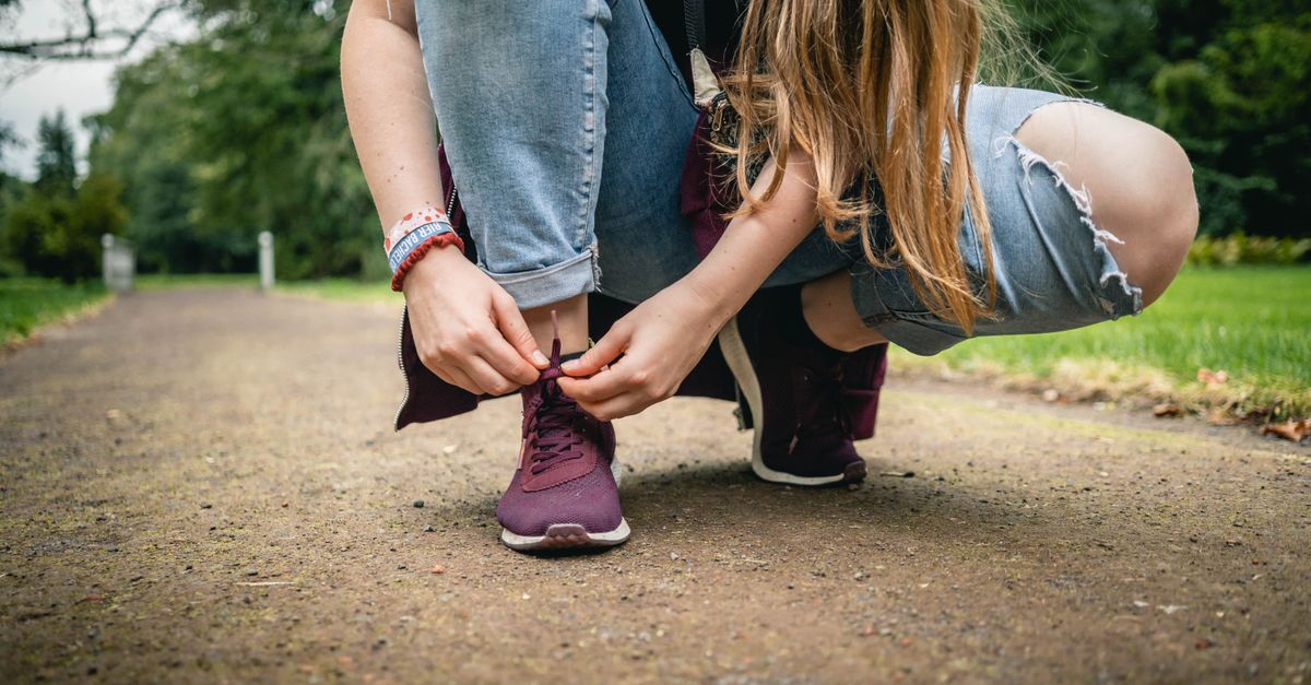 Close-up of a young woman tying purple sneakers on a path in a park, denim style.