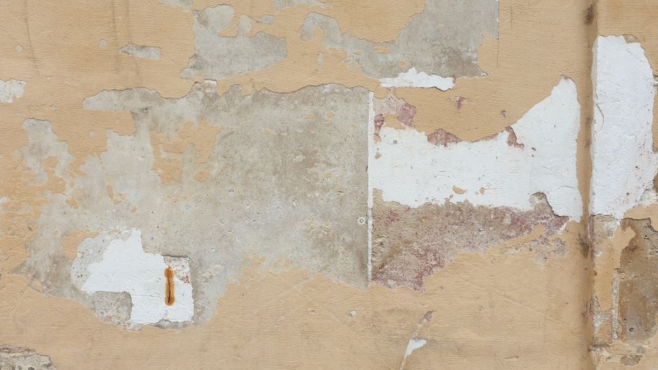 Damaged interior wall with peeling paint, plaster loss and damp staining indicating moisture ingress