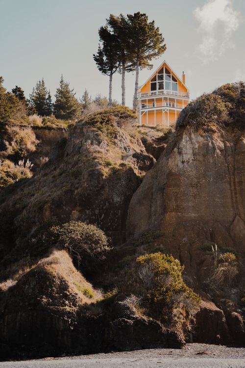Free A vibrant yellow house perched atop a rugged hill nestled amid lush greenery. Stock Photo