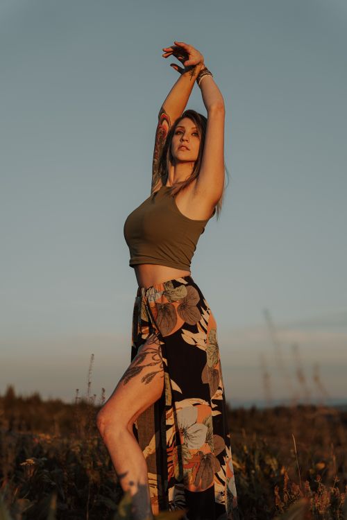 Free A fashionable woman with tattoos poses confidently in a field during sunset, showcasing her chic style. Stock Photo