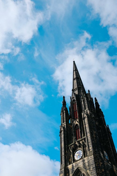 Free Impressive gothic clock tower with ornate details reaching into a clear blue sky. Stock Photo