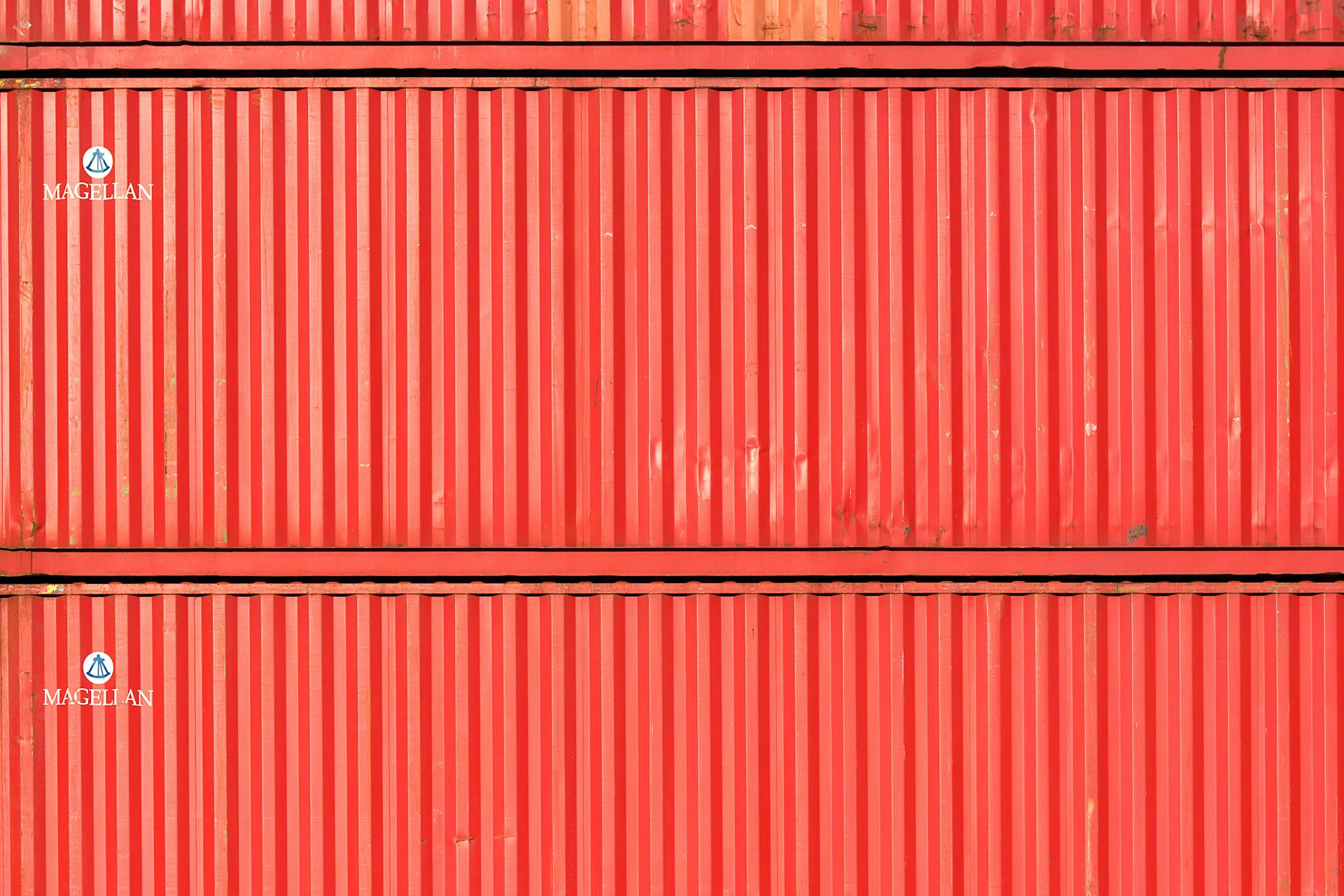 Close-up of stacked red cargo containers, providing a vibrant industrial texture.