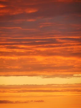 Beautiful vibrant orange sunset sky with layers of clouds creating a serene twilight mood.