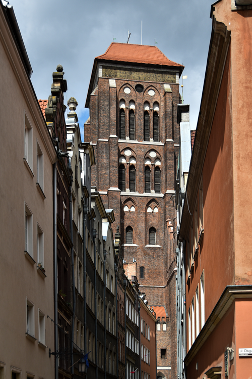 Free Low angle view of a historic basilica tower in Gdansk, framed by traditional urban facades under cloudy skies. Stock Photo