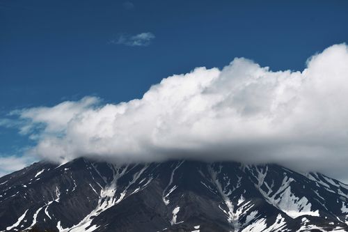 Free Dramatic view of a snow-capped mountain peak enveloped by thick clouds under a clear blue sky. Stock Photo