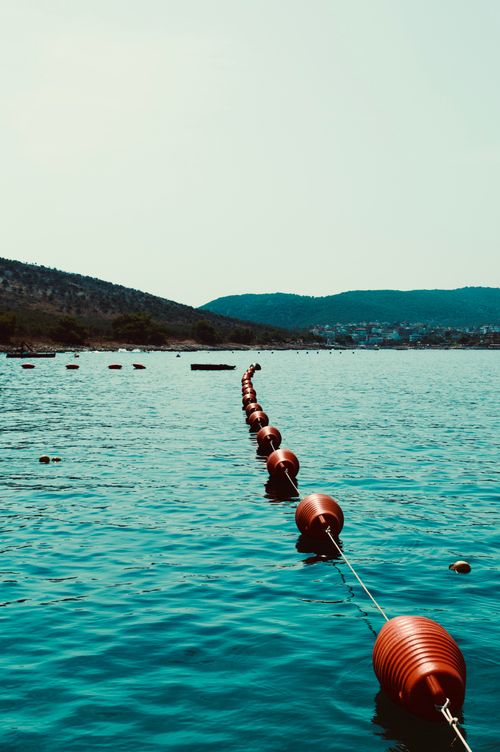 Free Calm water scene with red buoys forming a line across the tranquil sea and scenic hills. Stock Photo