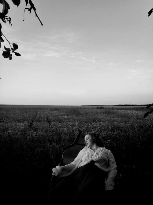 Grayscale Photo of a Woman Sitting on a Chair on Grass Field