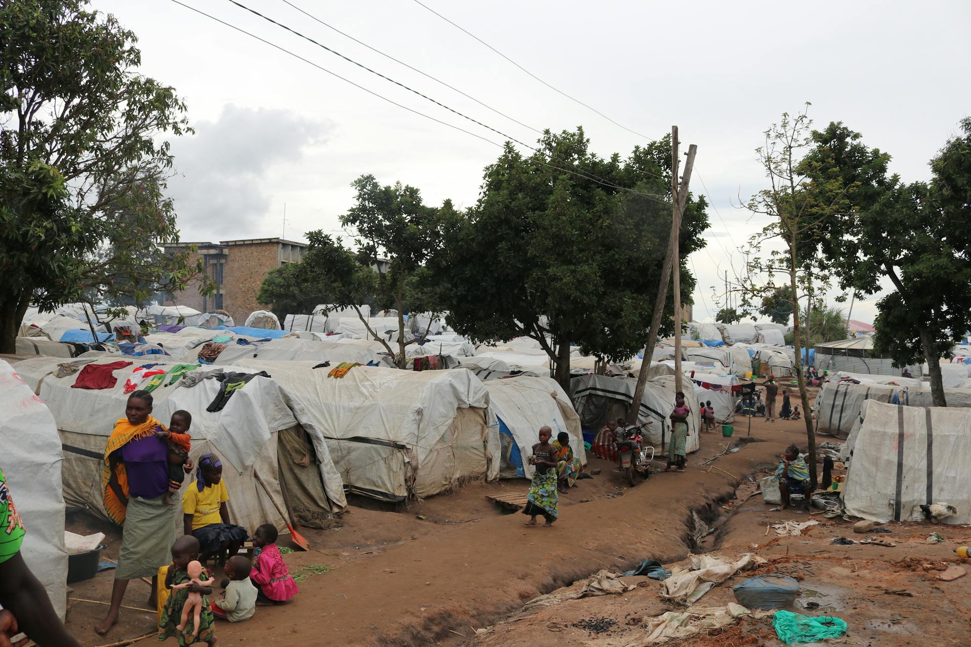 Overview of an African refugee camp with families and tents under trees, daytime