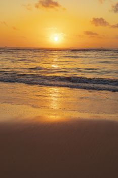 Serene beach at sunset with golden skies reflecting on gentle waves.