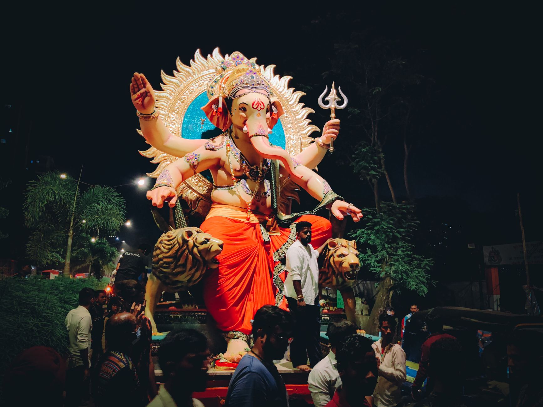 Joyful celebration of Ganesh Chaturthi with people gathering around a vibrant Ganesha idol at night.