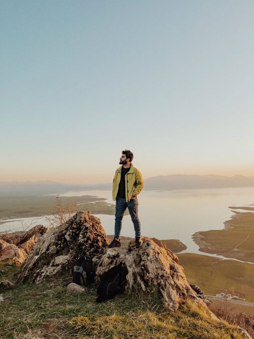 Free A man stands on a rocky outcrop overlooking serene Qurago landscape at dusk. Stock Photo
