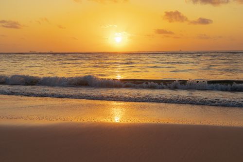 Free A tranquil ocean sunset with gentle waves reflecting the golden hues of the setting sun. Stock Photo