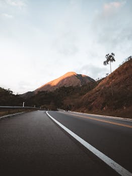 A picturesque mountain road under a beautiful sunset glow, framed by distant peaks.