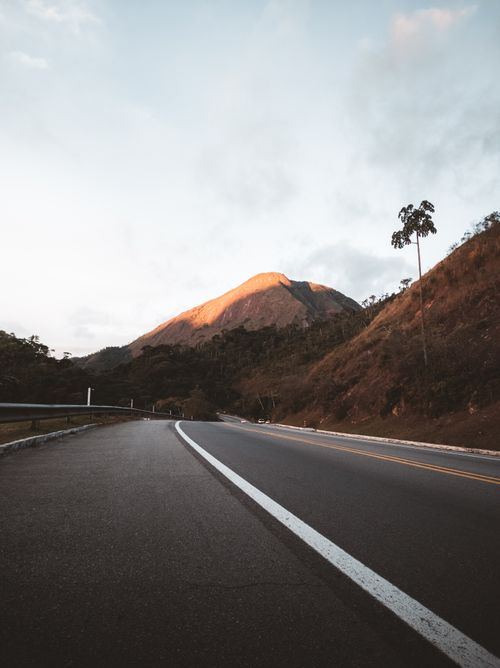 Free A picturesque mountain road under a beautiful sunset glow, framed by distant peaks. Stock Photo