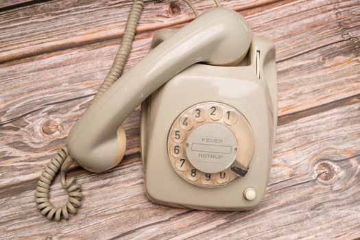 Retro rotary phone with dial on rustic wooden surface, nostalgic feel.