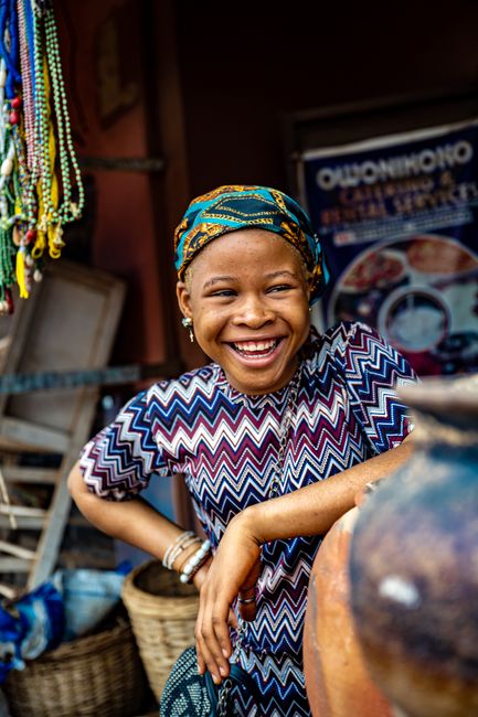 A joyful African woman in traditional attire, showcasing cultural diversity in a vibrant market setting.