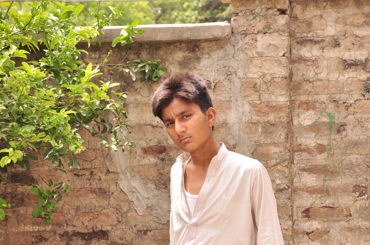 young man with a mandarin collar shirt standing by a rustic wall outdo