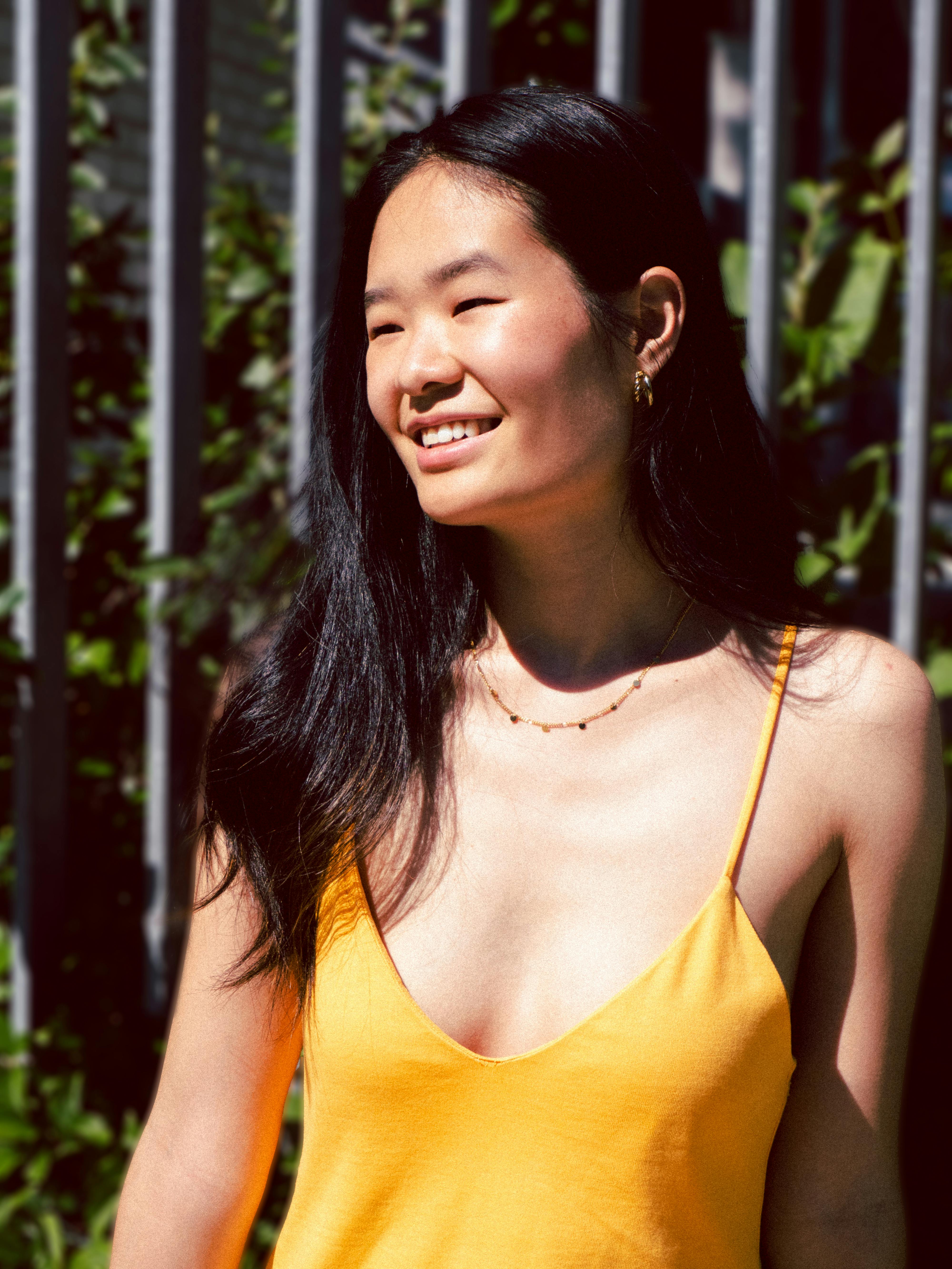 A cheerful woman in a yellow top smiles under the sun, embracing the outdoor vibes.