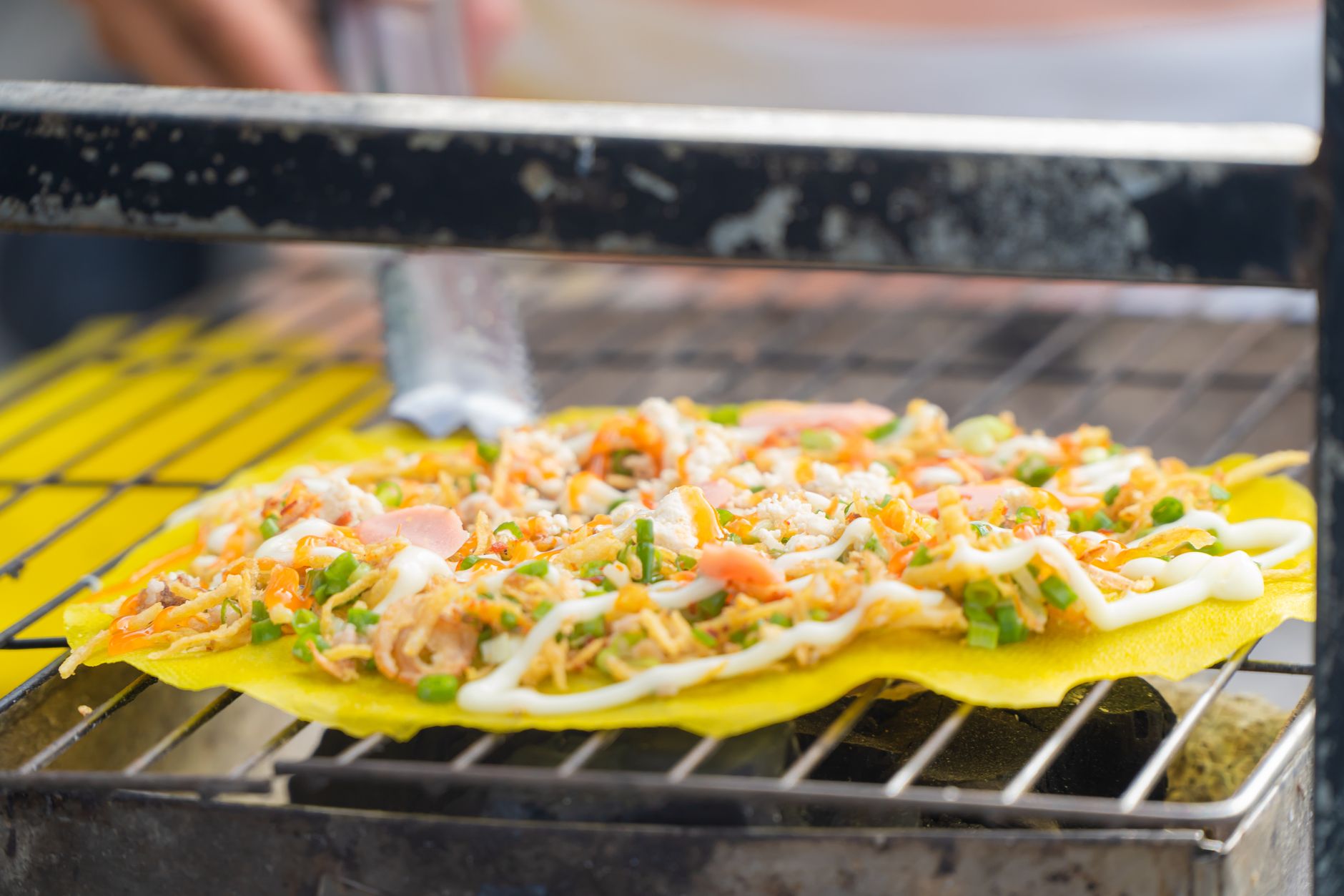 A close-up of Vietnamese Bánh Tráng Nướng being grilled, featuring fresh ingredients and vibrant colors.