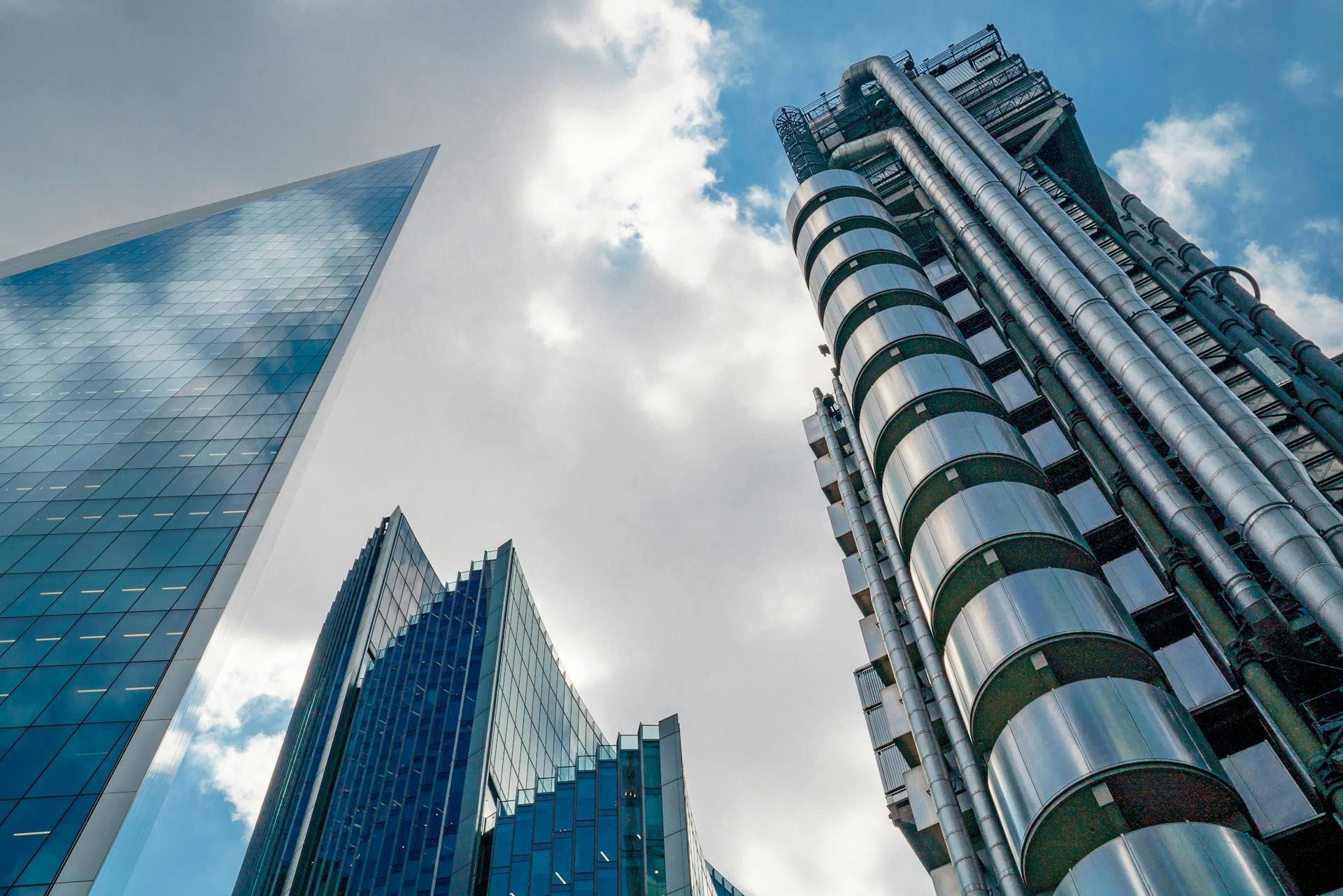 Low angle view of futuristic skyscrapers in London's financial hub under a partly cloudy sky.